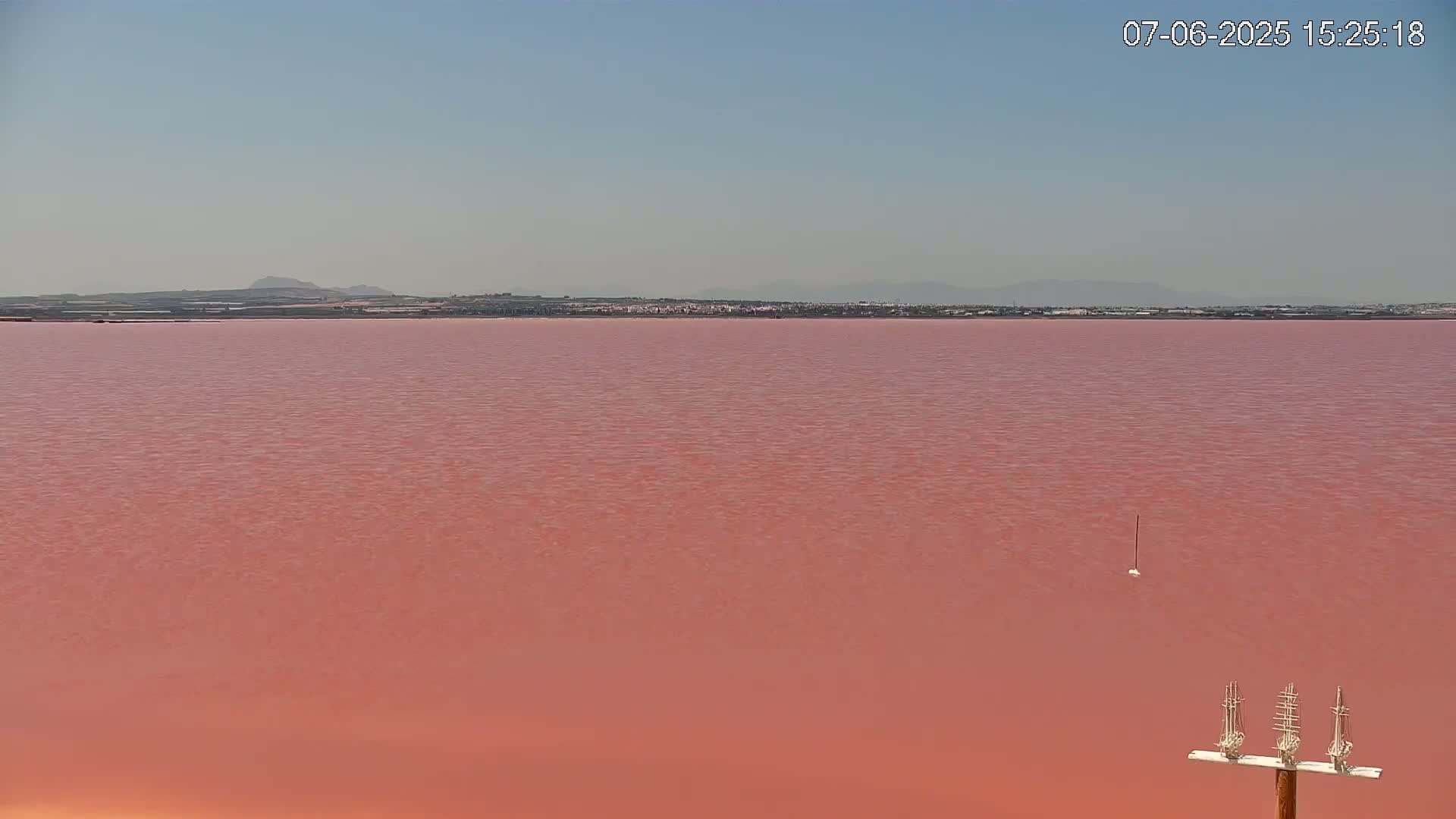 A large pink lake stretches to a distant shoreline under a clear sky.