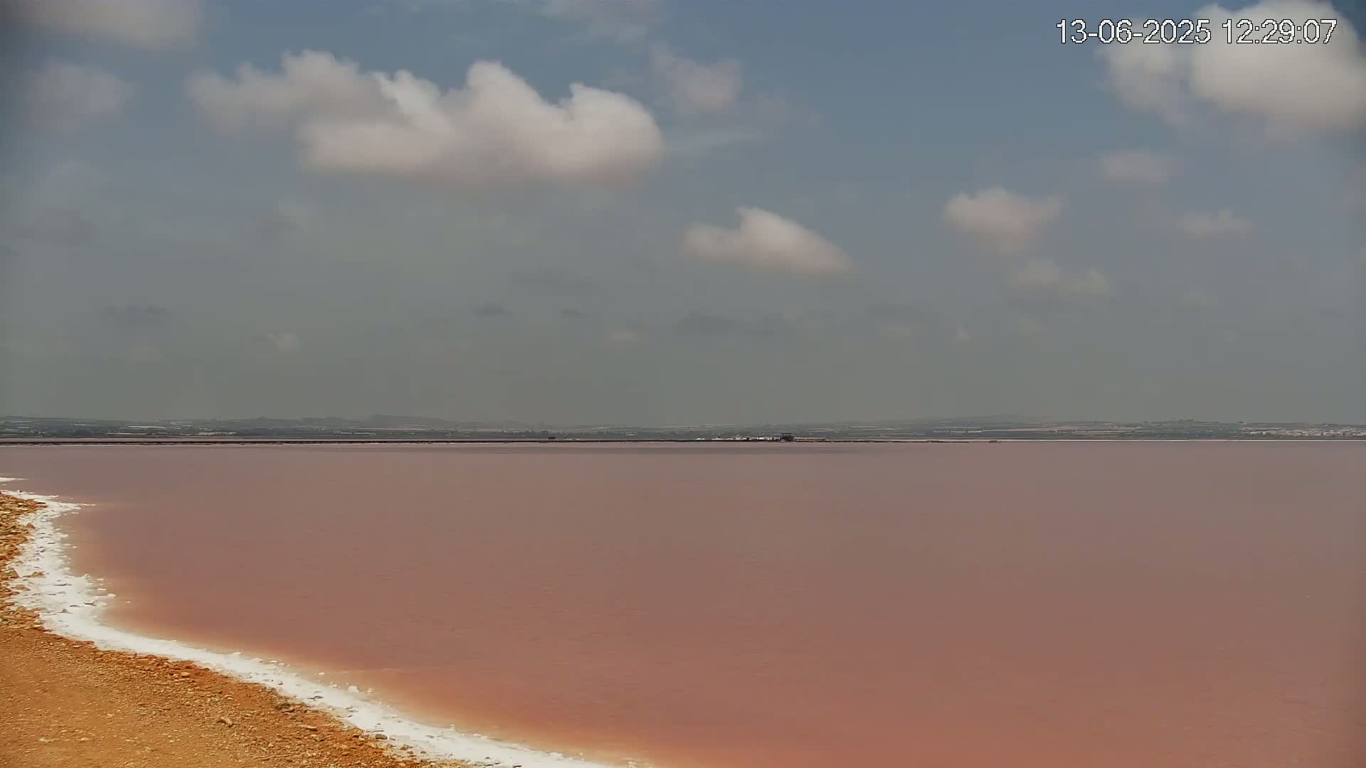 A pink lake stretches to a distant horizon under a partly cloudy sky.
