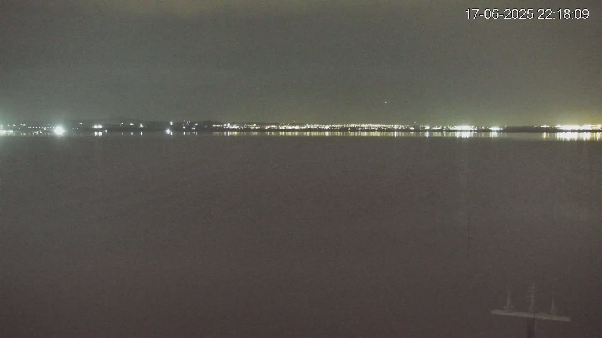 A dark, calm body of water reflects the lights of a distant city at night.