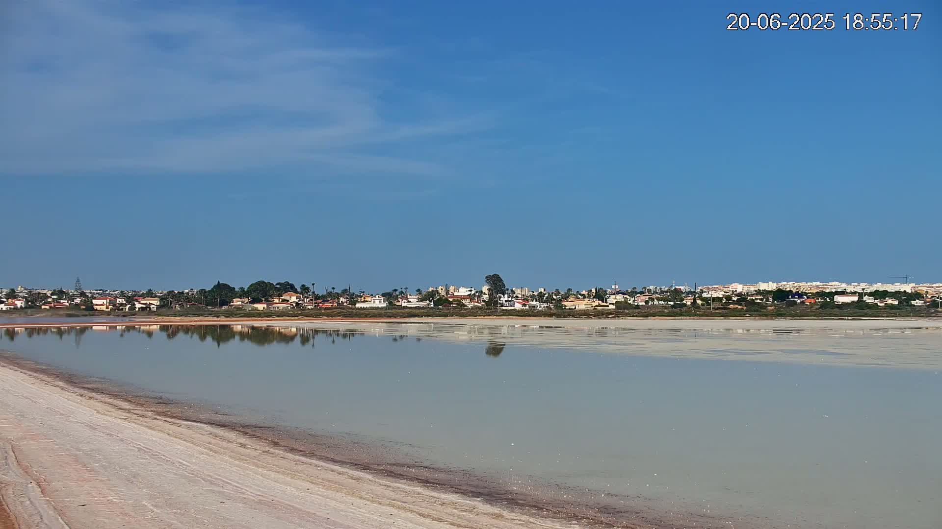 A calm, pale-colored body of water reflects a distant town under a clear blue sky.