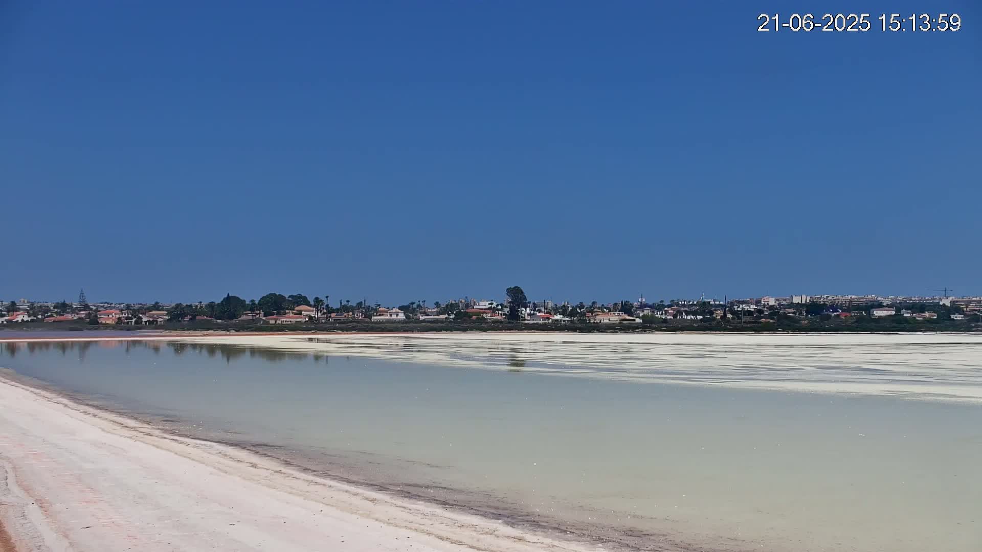 A calm, light-green body of water stretches out before a distant town under a clear blue sky.