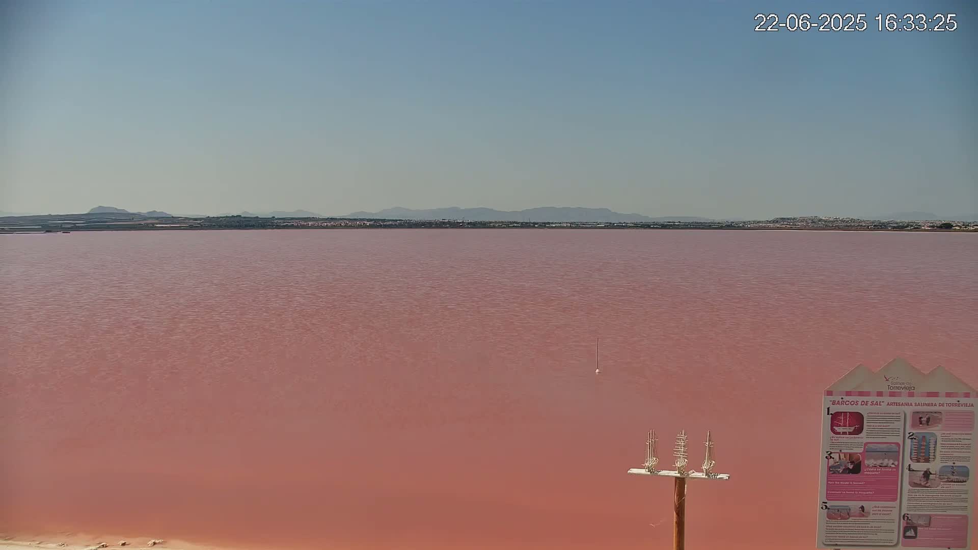 A pinkish-red lake stretches to a distant, hazy mountain range under a clear sky.