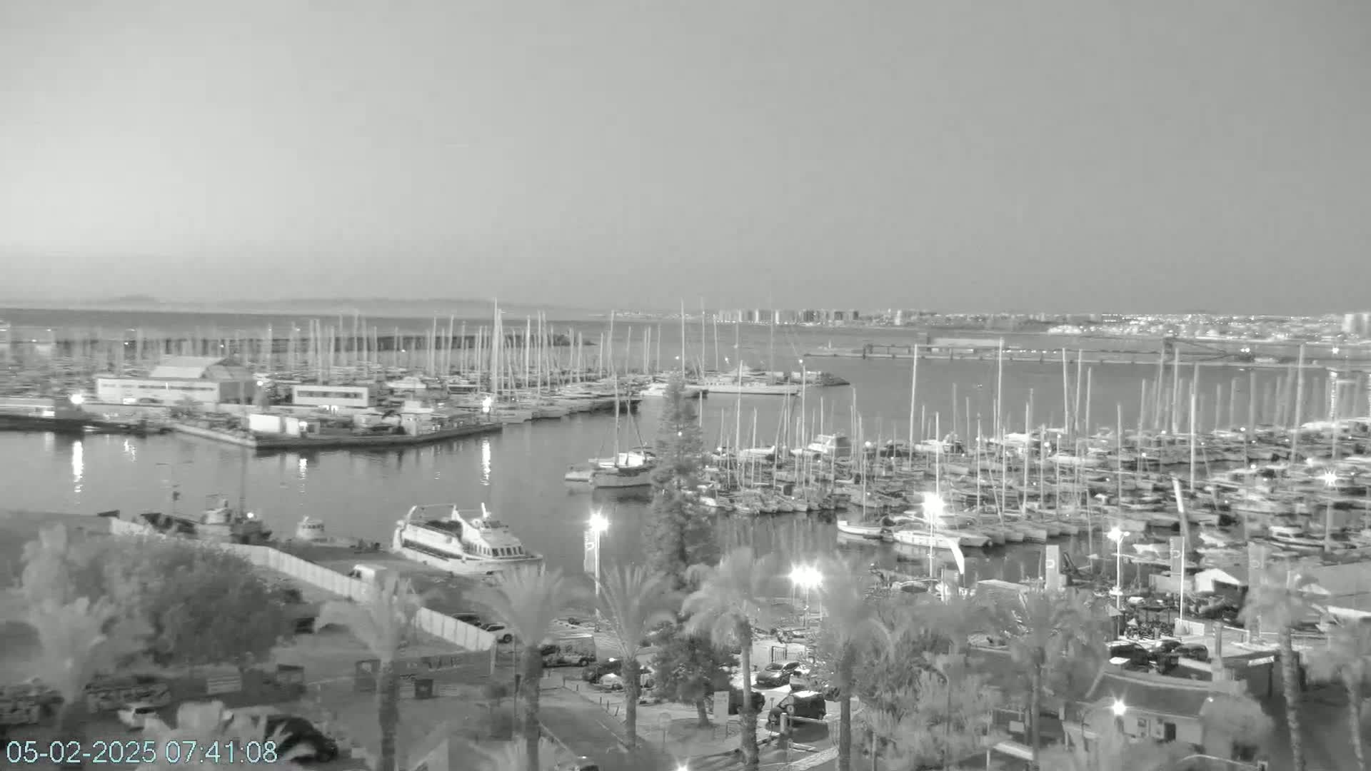 A large marina filled with numerous boats and yachts is shown at twilight under a clear sky.