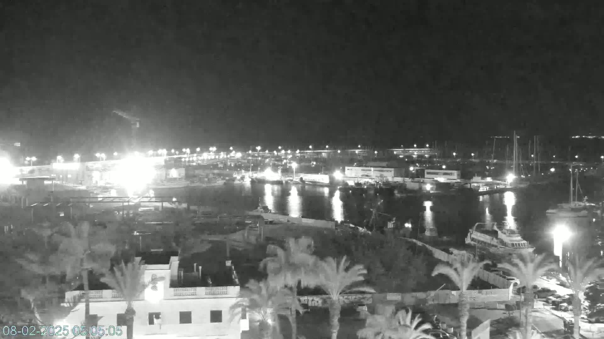 A nighttime, low-light view of a harbor filled with boats and buildings, illuminated by artificial lights.