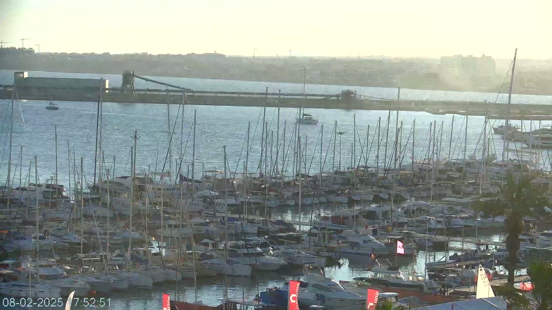 A large marina filled with numerous sailboats and motorboats is seen on a calm, hazy day.