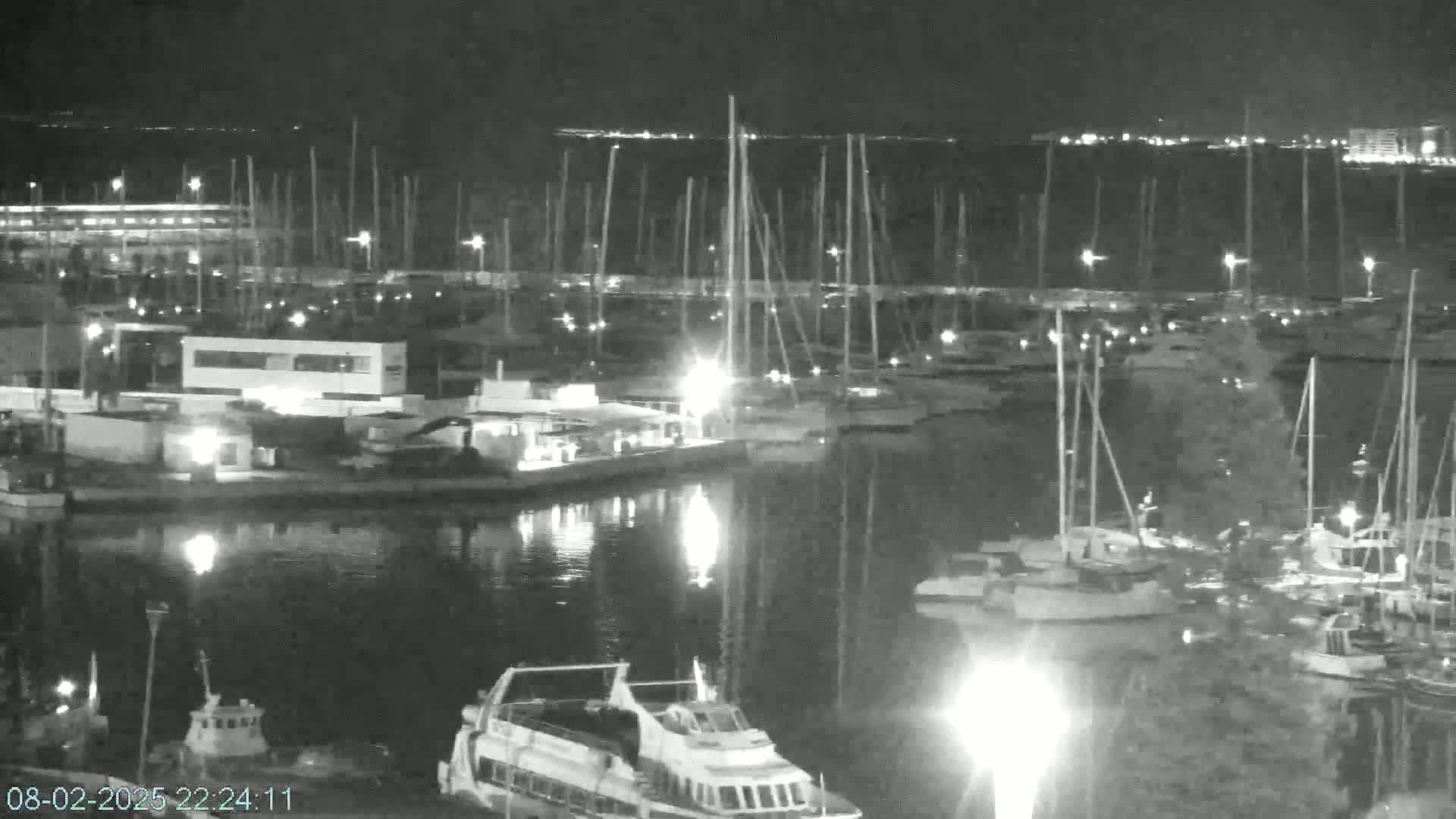 A nighttime, low-light view of a marina filled with sailboats and motorboats, with calm water reflecting the lights.