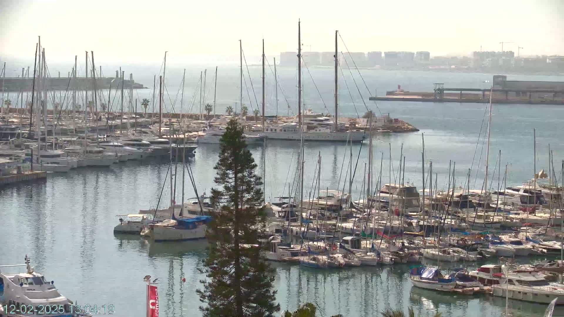 A marina filled with numerous sailboats and motorboats on a hazy day.