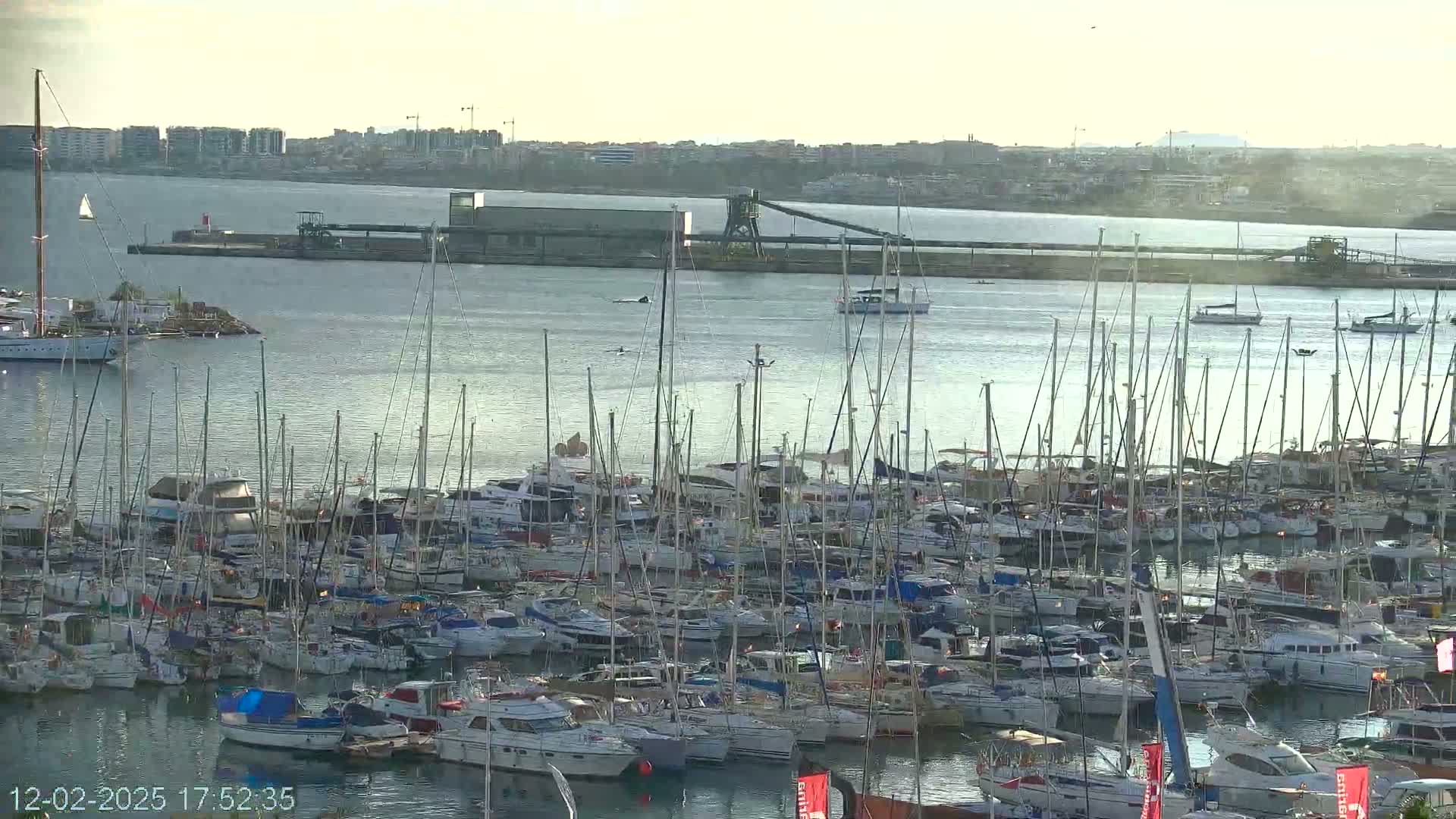 A marina filled with numerous sailboats and motorboats is seen on a calm, hazy day.