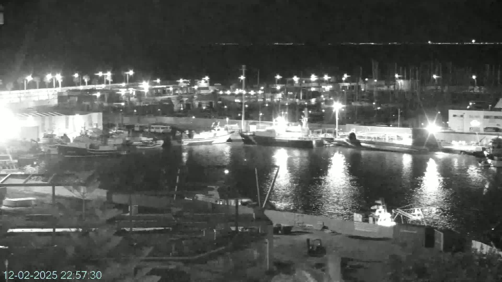 A nighttime view of a harbor filled with boats, illuminated by lights reflecting on calm water.