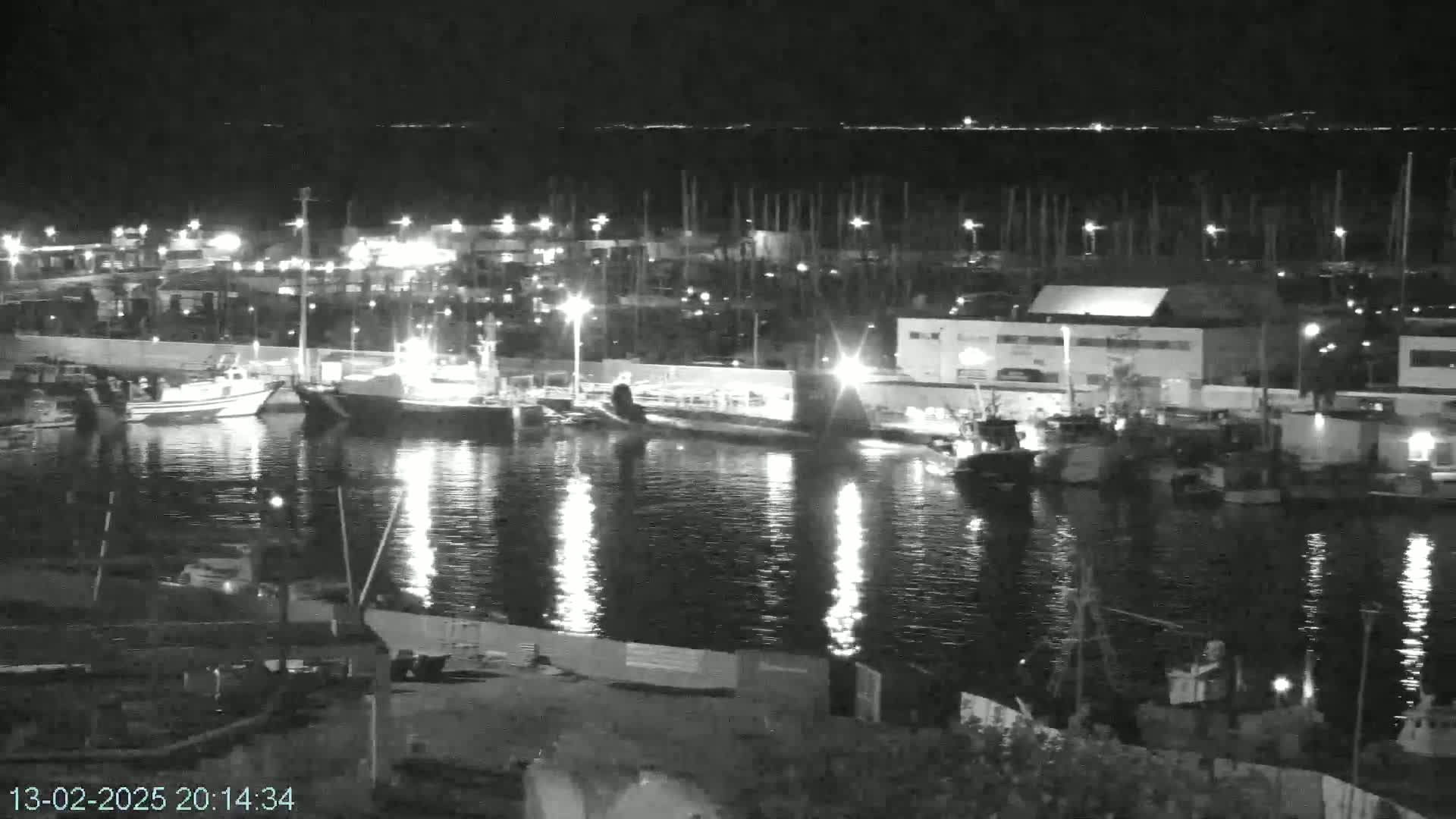 A nighttime view of a harbor filled with docked boats and illuminated by lights reflecting on calm water.