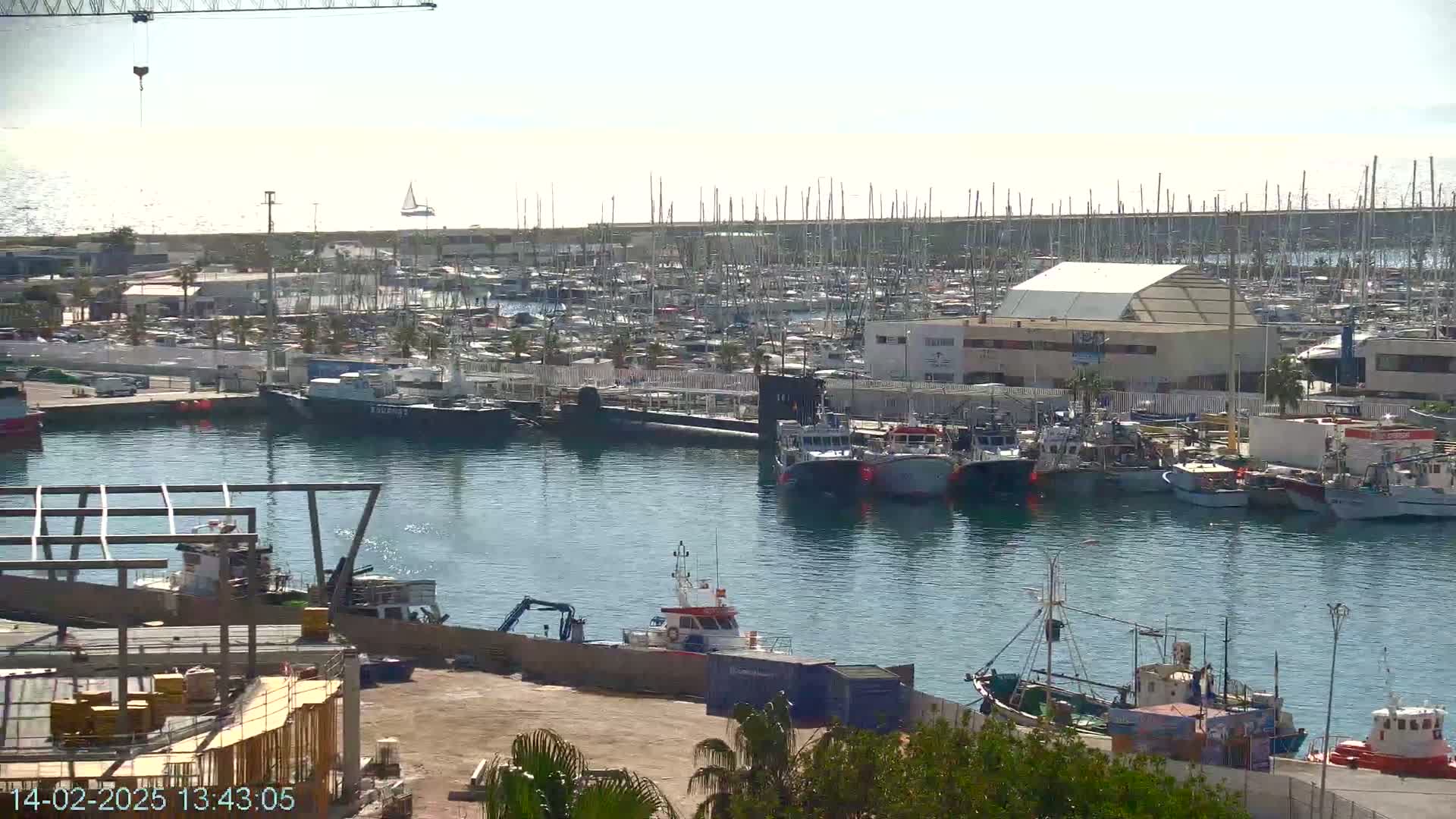 A harbor filled with numerous boats and ships under a sunny sky, with a construction site visible in the foreground.