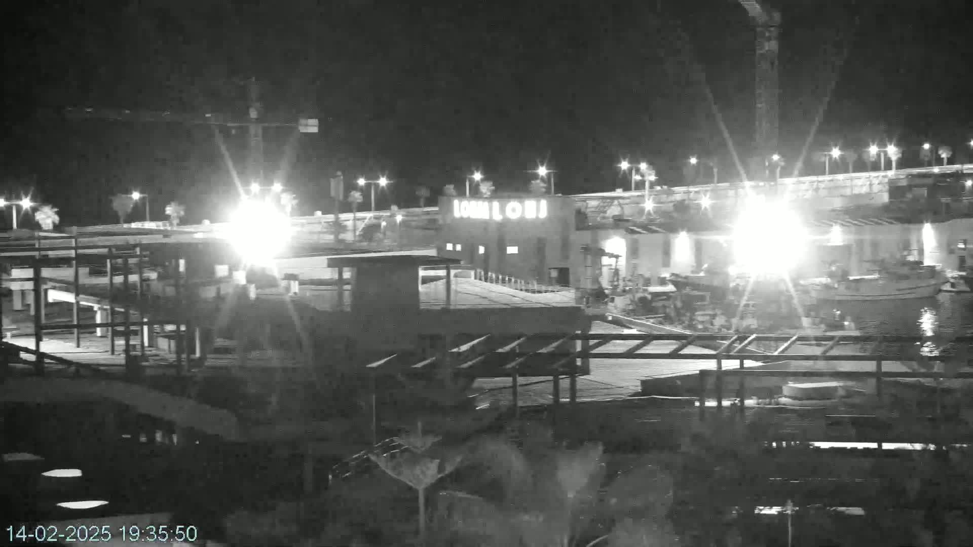 A nighttime, low-light view of a waterfront area with buildings, boats, and some construction visible.