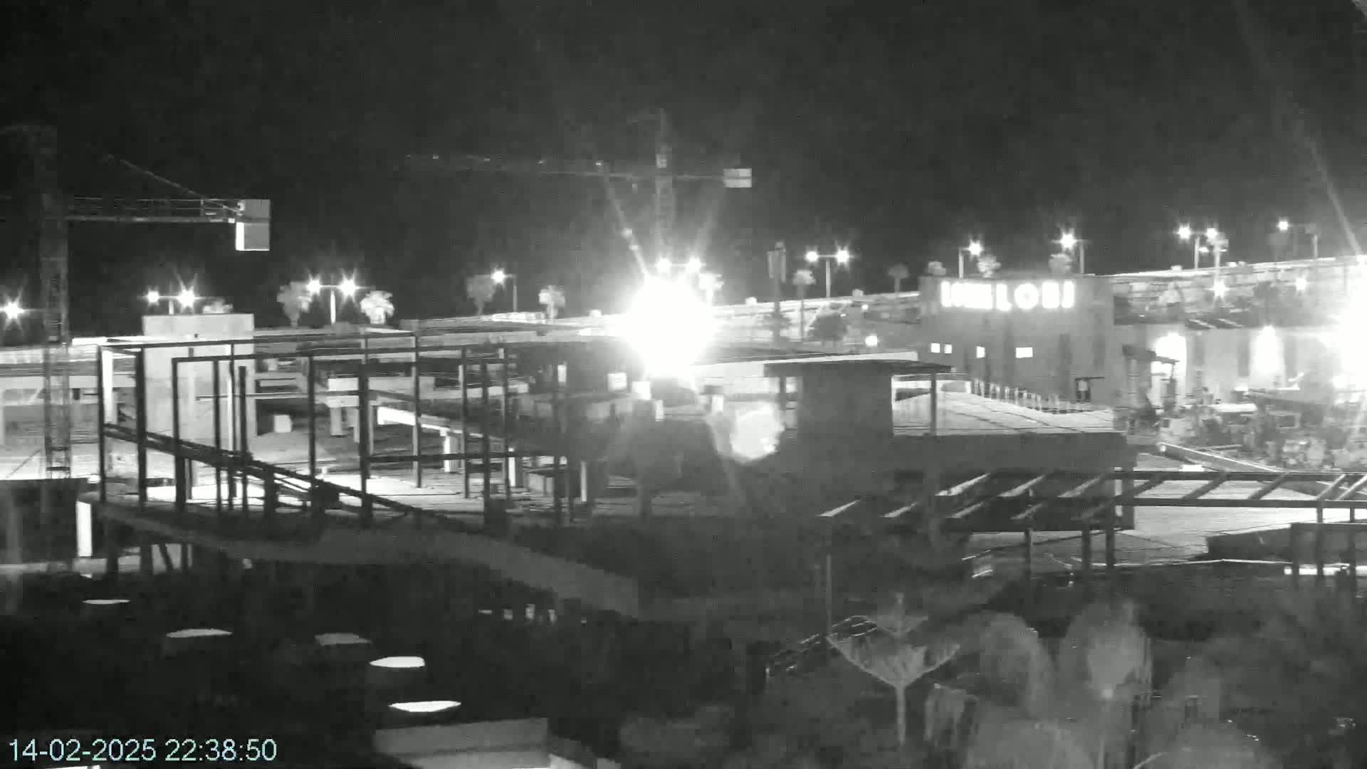 A nighttime, black-and-white view of a construction site with a crane, some buildings, and bright lights.