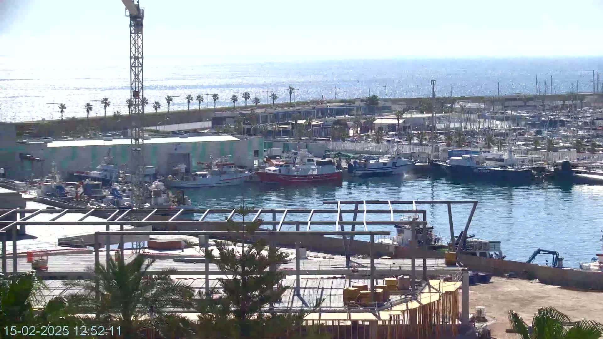 A harbor filled with numerous boats and ships under a sunny sky, with a construction site in the foreground.