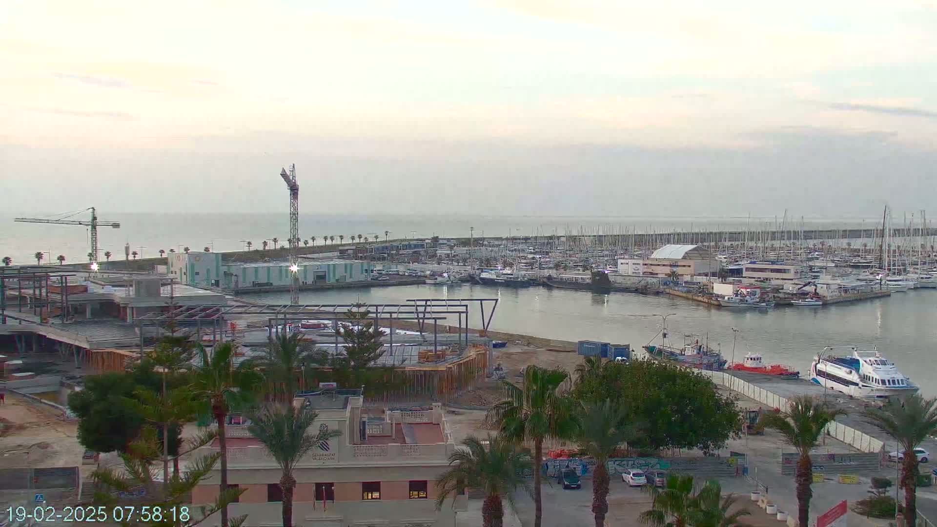 A marina filled with boats under an overcast sky, with construction underway on a building nearby.