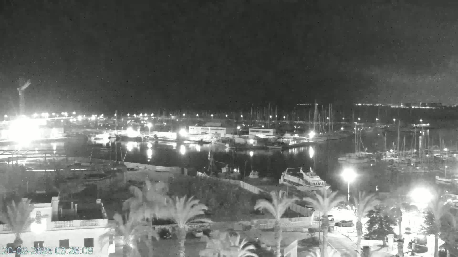 A nighttime view of a harbor filled with boats, lit by artificial lights under a dark, clear sky.