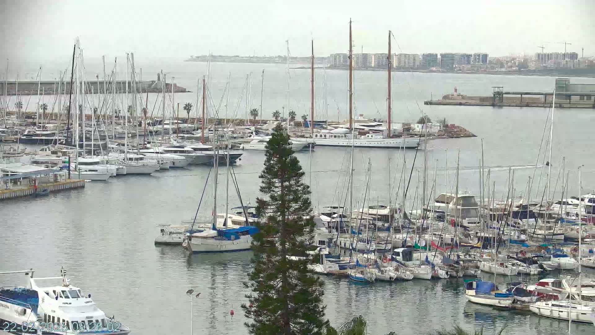A large marina filled with numerous sailboats and motorboats under an overcast sky.
