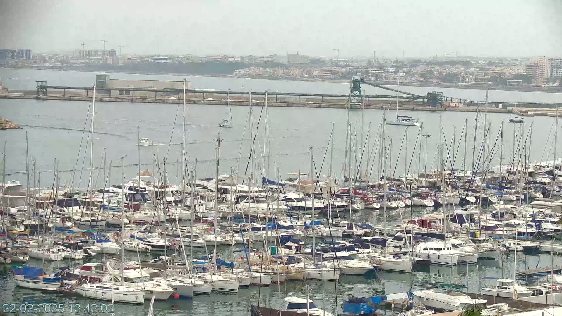 A large marina filled with numerous sailboats and motorboats is seen on an overcast day.