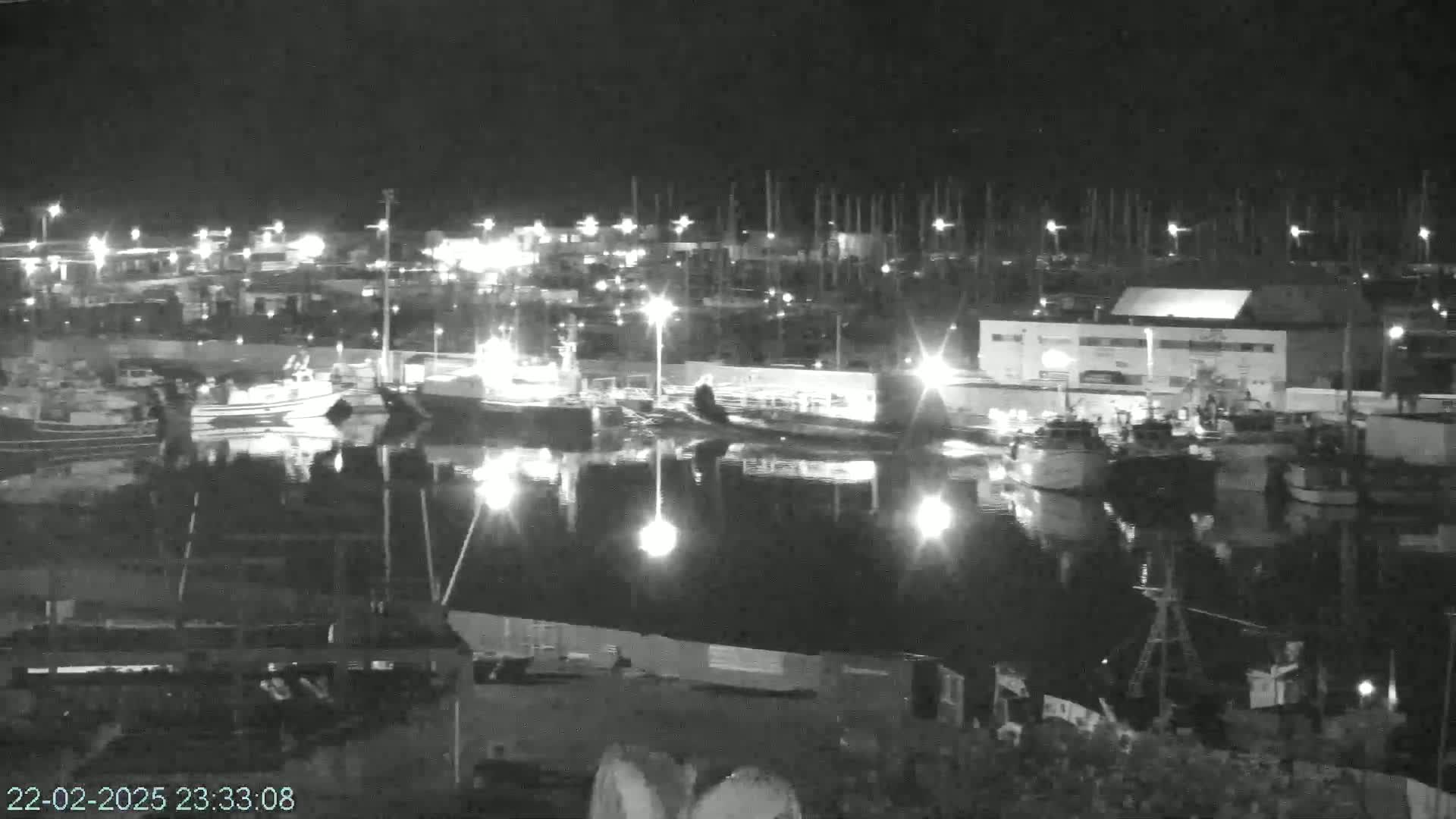 A nighttime, low-light view of a harbor filled with boats, reflecting lights onto calm water.