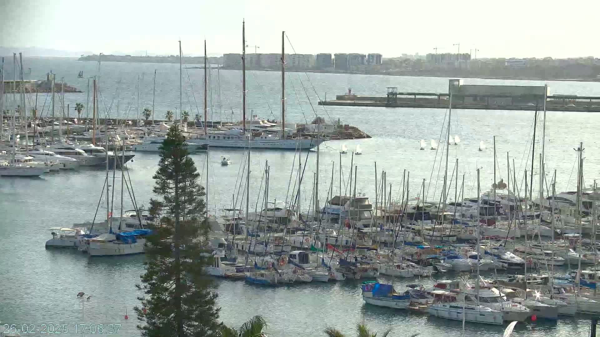A marina filled with numerous sailboats and motorboats under a hazy, overcast sky.