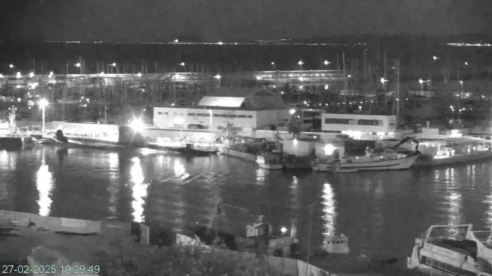 A nighttime view of a harbor filled with boats and buildings, illuminated by lights reflecting on calm water.