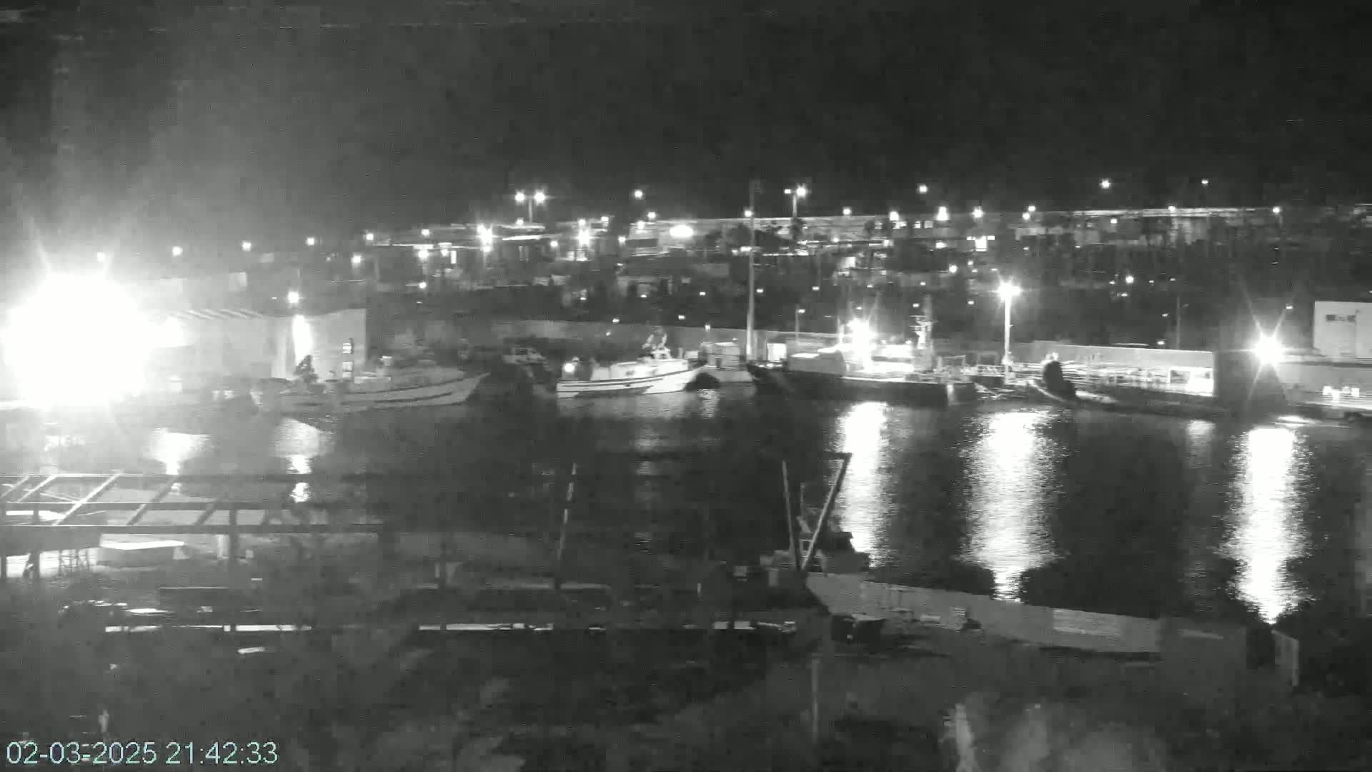 A nighttime, low-light view of a harbor shows several boats docked, with lights reflecting on the calm water.