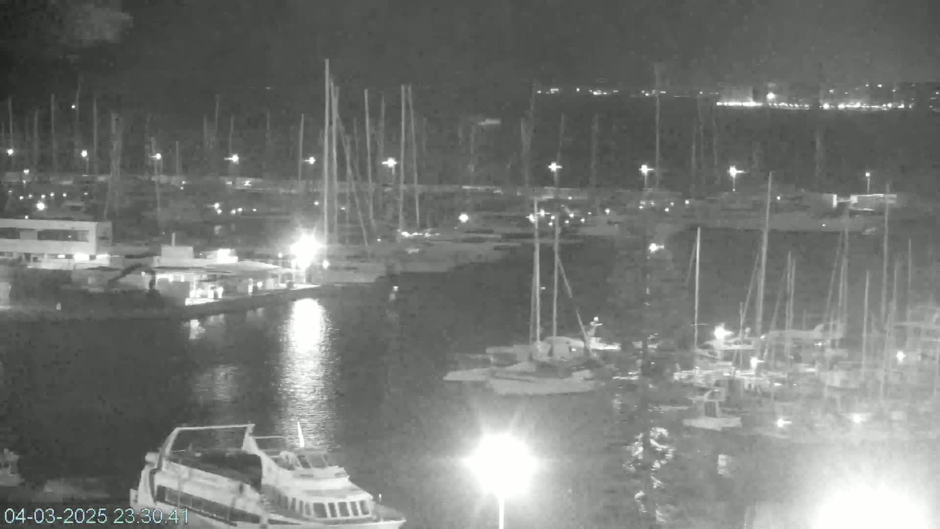 A nighttime, low-light view of a marina filled with numerous boats and yachts, some illuminated by lights.