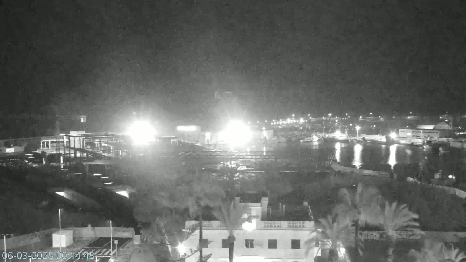 A nighttime, low-light view of a harbor with boats and buildings, partially obscured by what appears to be light rain or mist.