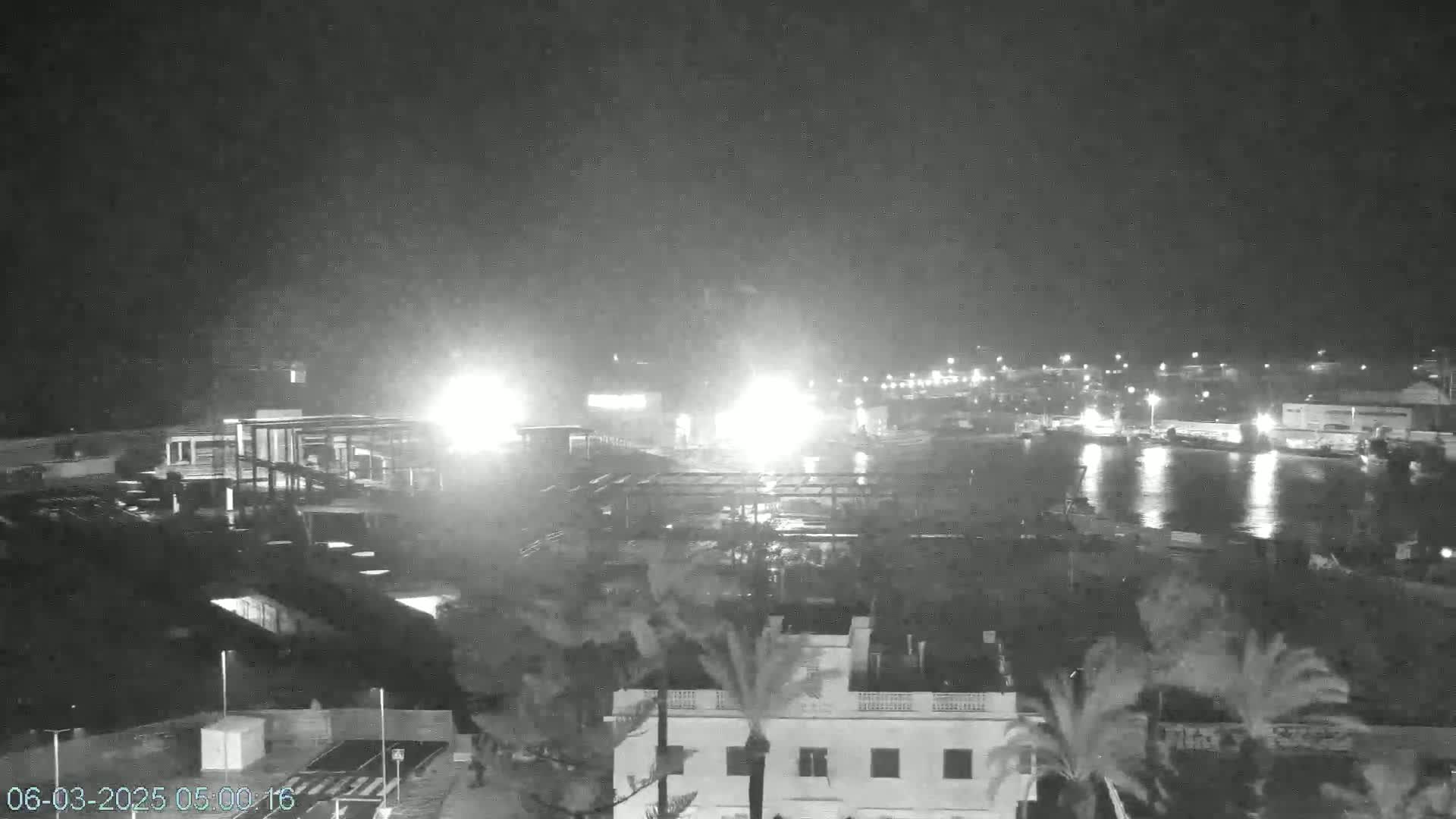 A nighttime view of a harbor with lights reflecting on the water under a slightly hazy sky.