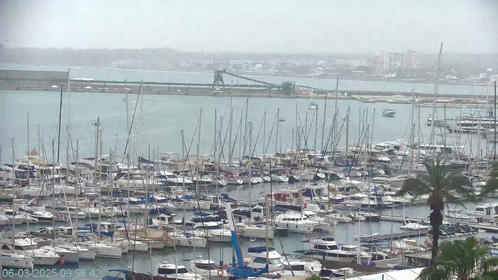 A marina filled with numerous sailboats and motorboats under an overcast sky.