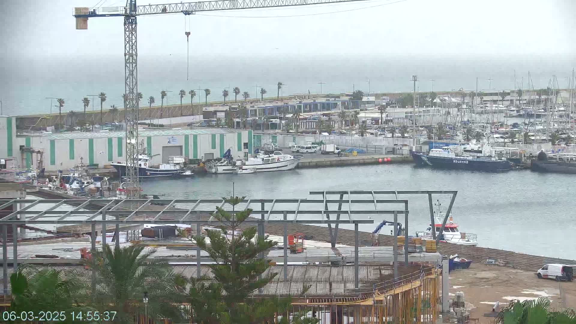 A construction site next to a harbor filled with boats on an overcast day.