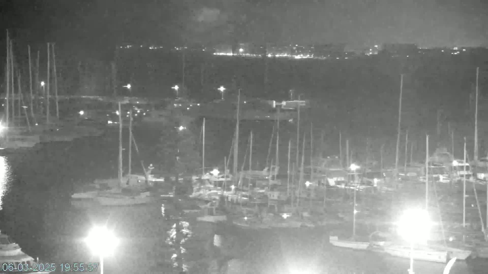 A nighttime, low-light view of a marina filled with numerous boats and yachts, with a city skyline faintly visible in the distance.