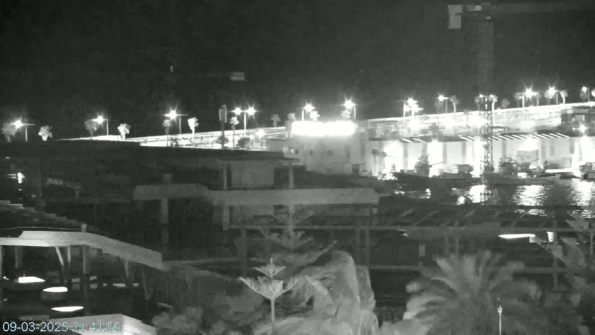 A nighttime view of a waterfront area with boats docked near a brightly lit bridge and buildings.