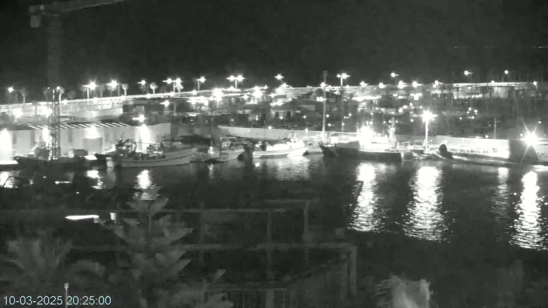 Several boats are moored in a harbor at night, illuminated by lights along the waterfront.