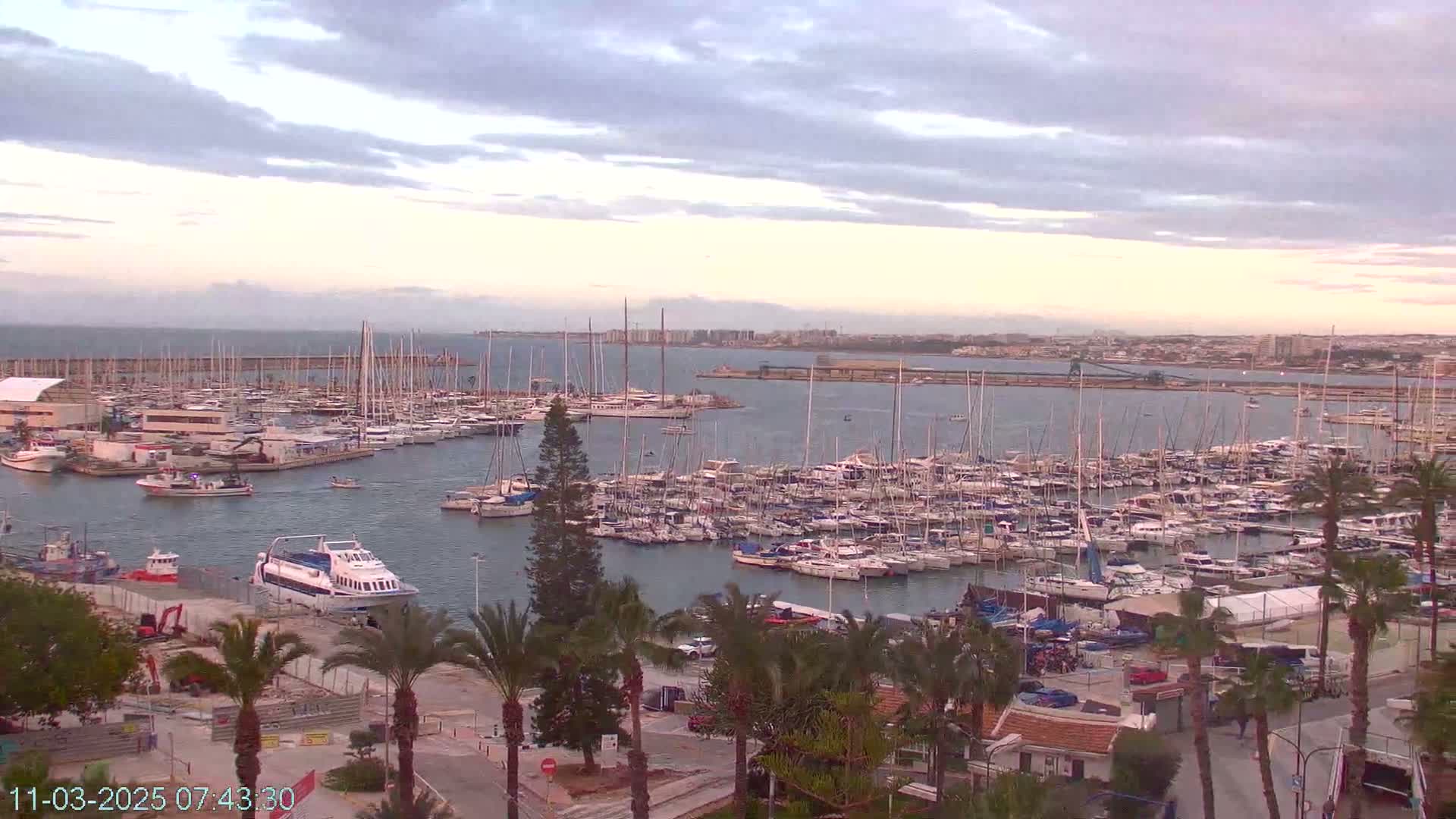A harbor filled with numerous sailboats and motorboats under a partly cloudy sky.