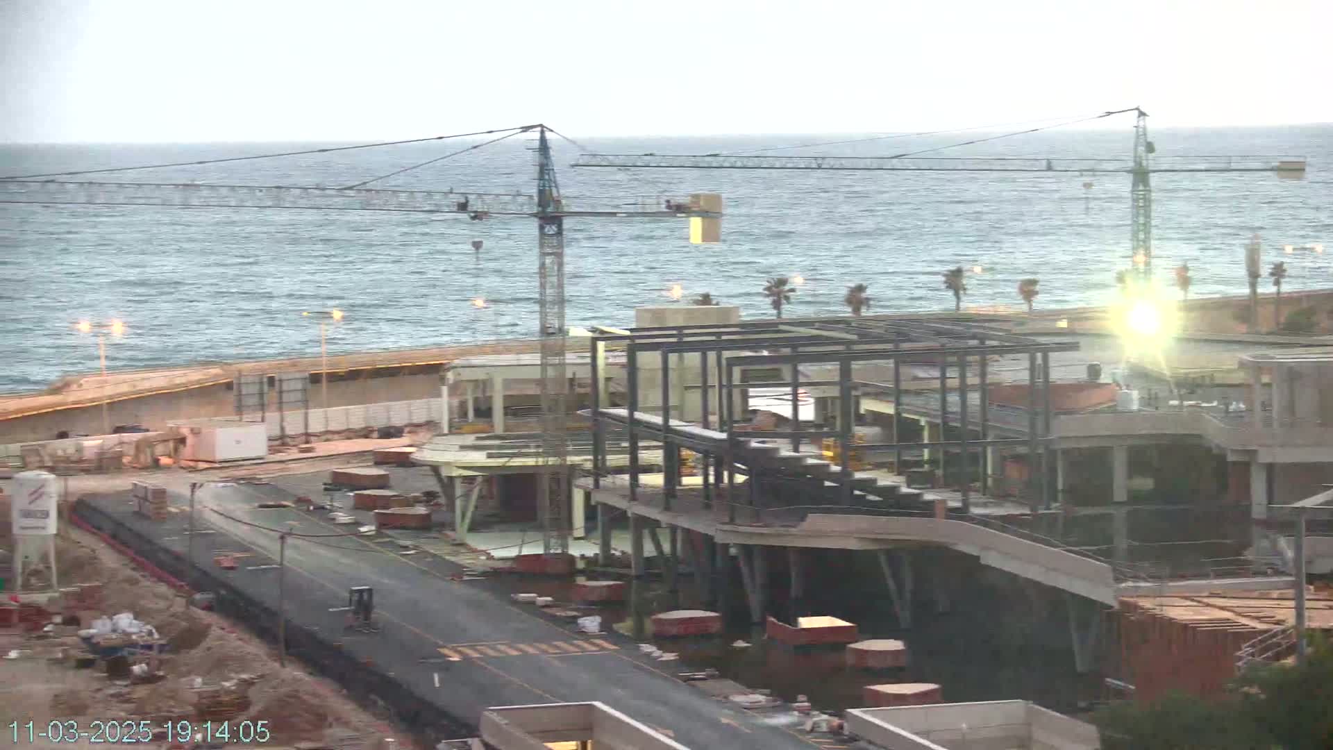A coastal construction site with cranes, partially built structures, and a choppy sea under an overcast sky.
