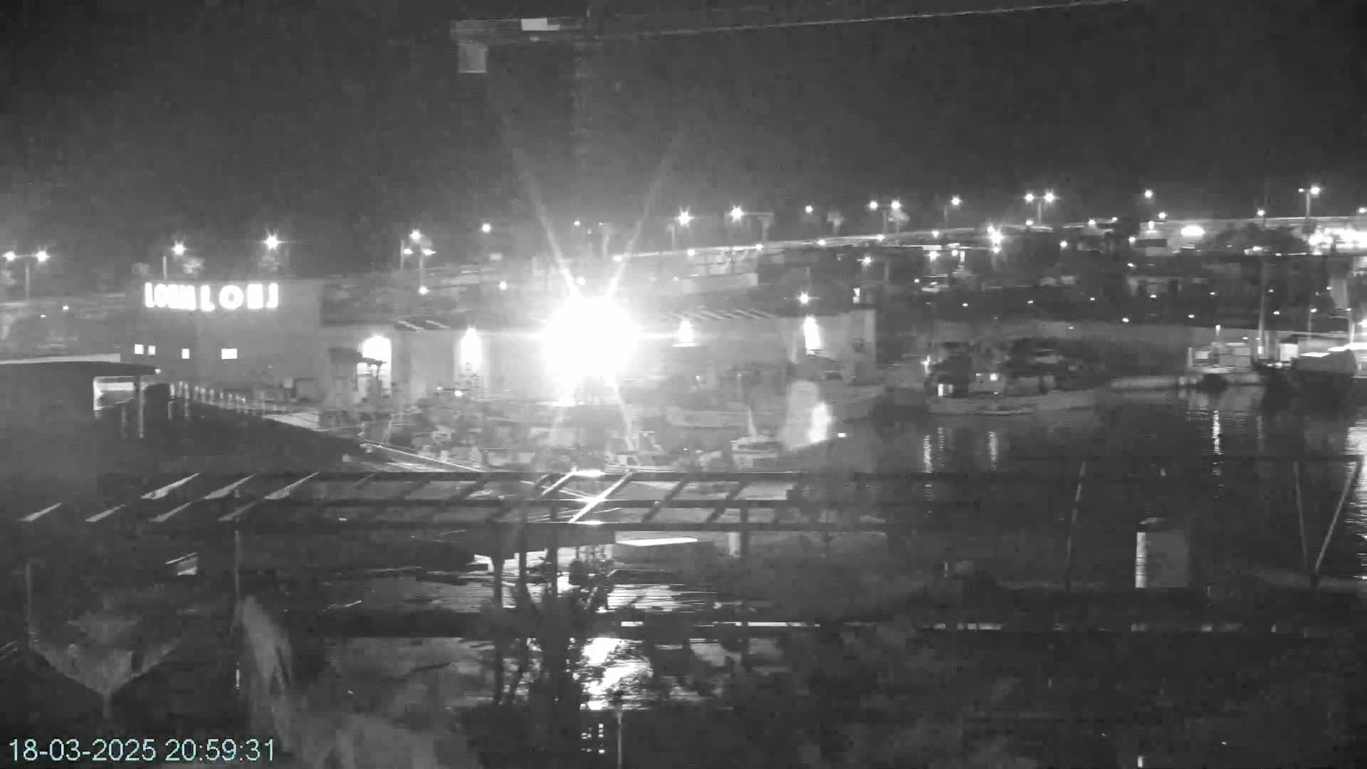 A nighttime, low-light view of a harbor with boats and a building illuminated by bright lights.