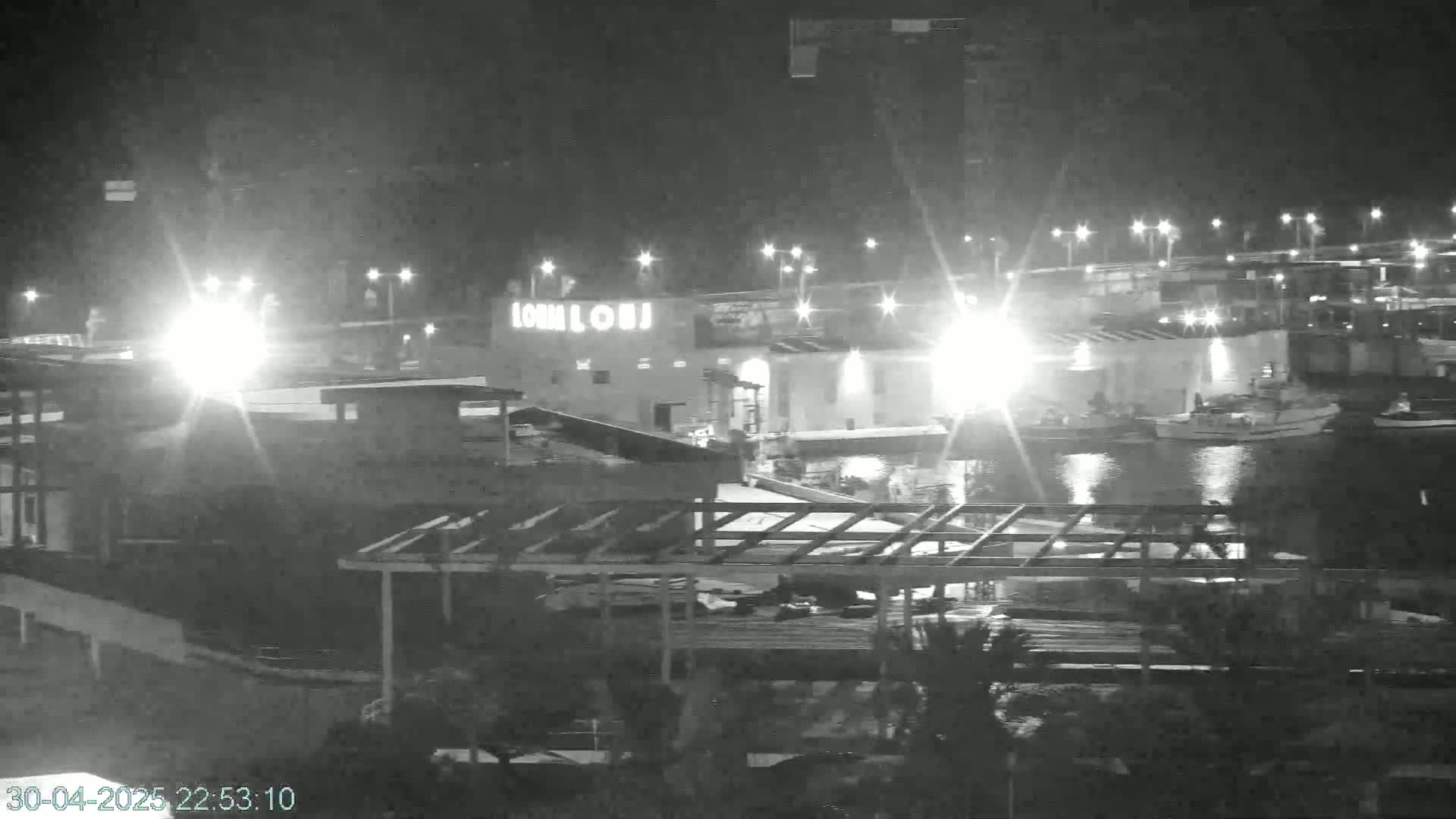 A nighttime, low-light view of a harbor with several boats moored near a building, with construction visible in the foreground.