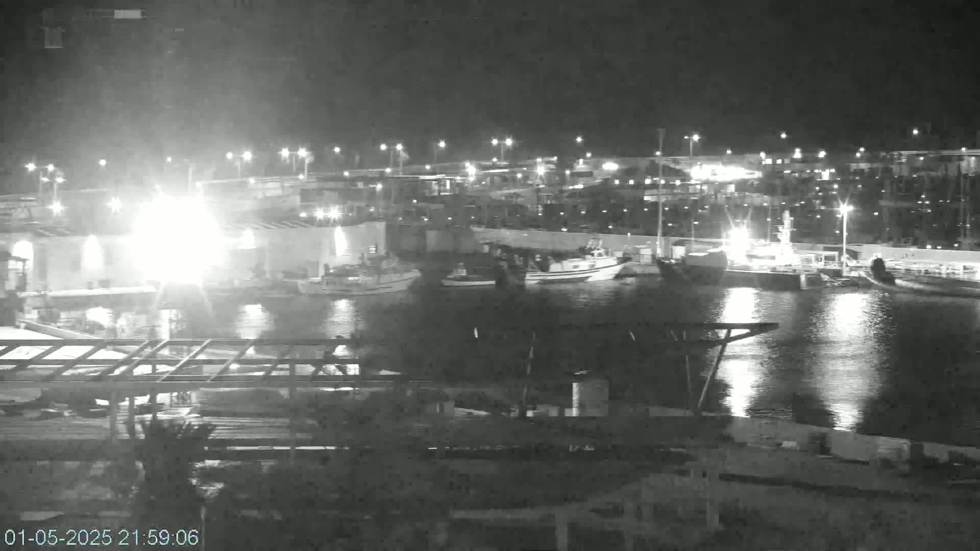 Several boats are moored in a harbor at night under clear skies, illuminated by artificial lights.