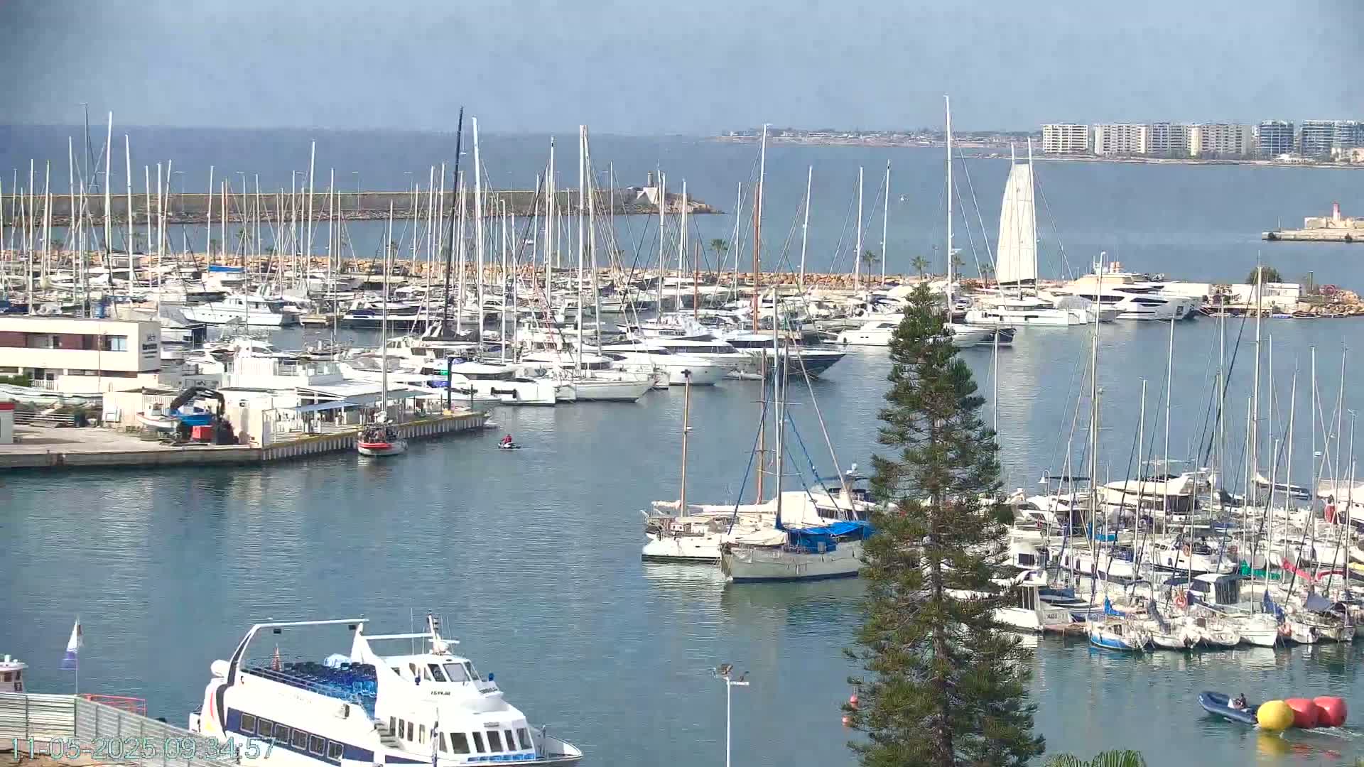 A marina filled with numerous sailboats and motorboats on a calm, sunny day.