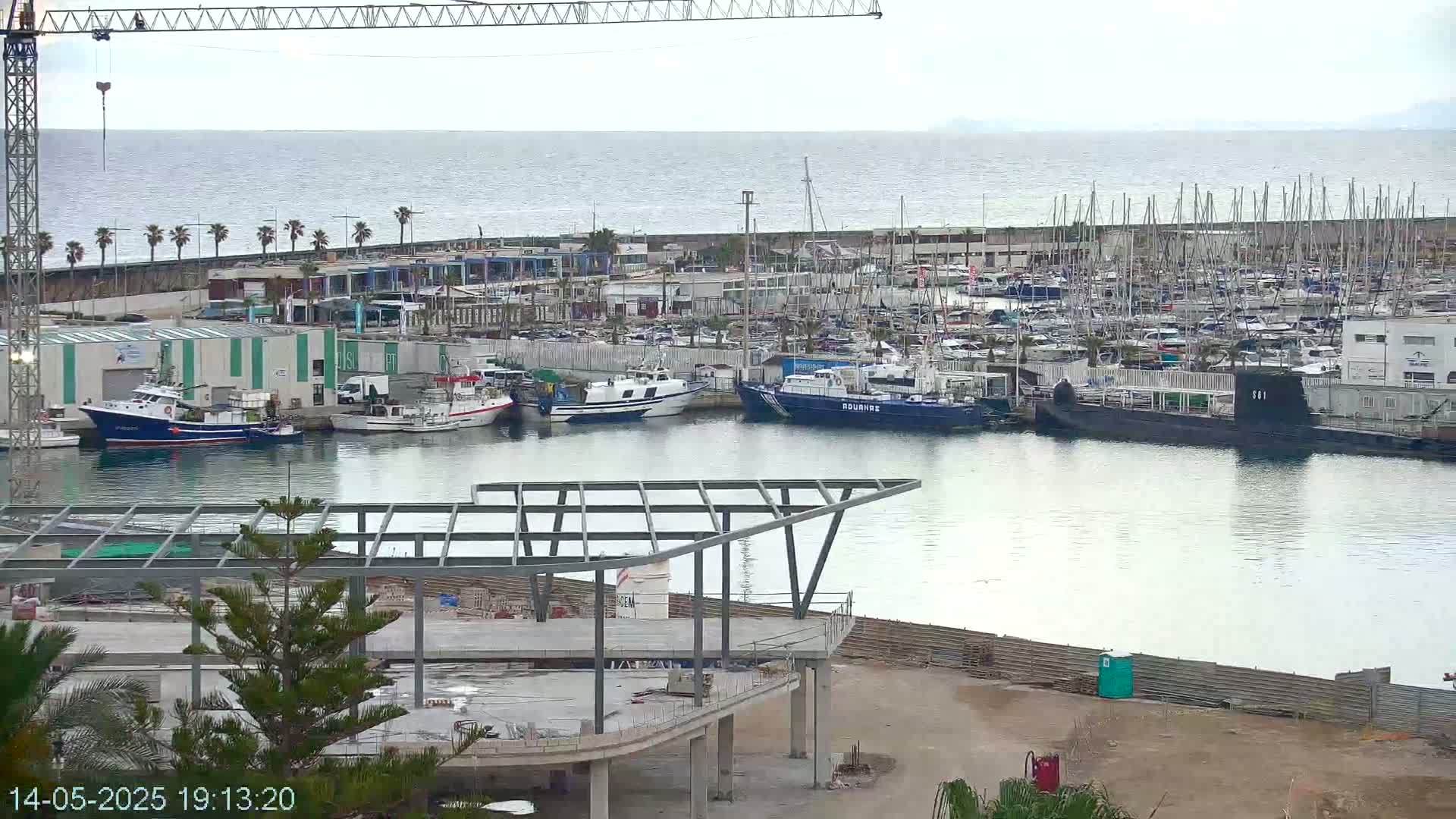 A harbor filled with numerous boats and a partially constructed building is seen under an overcast sky.