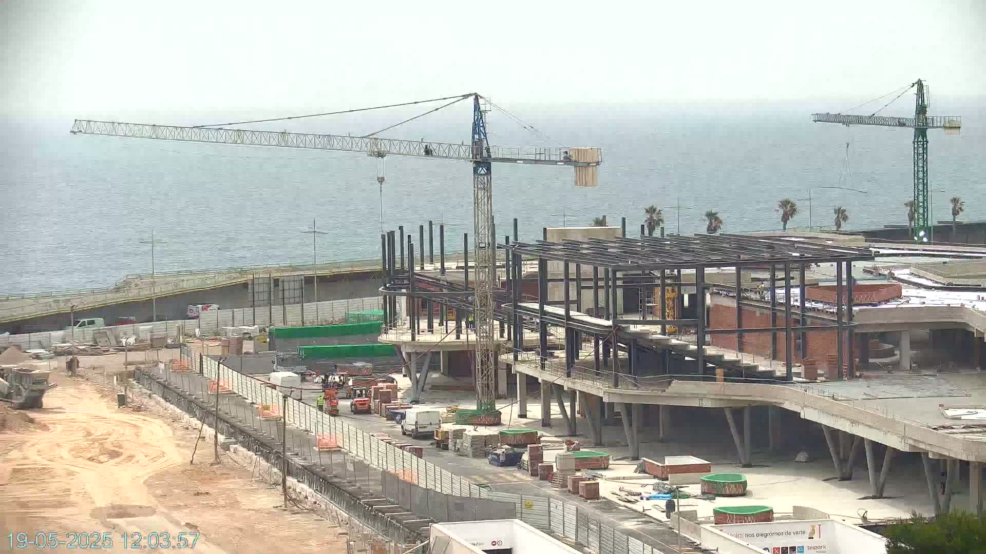 A large building under construction near the ocean on an overcast day, with two construction cranes visible.