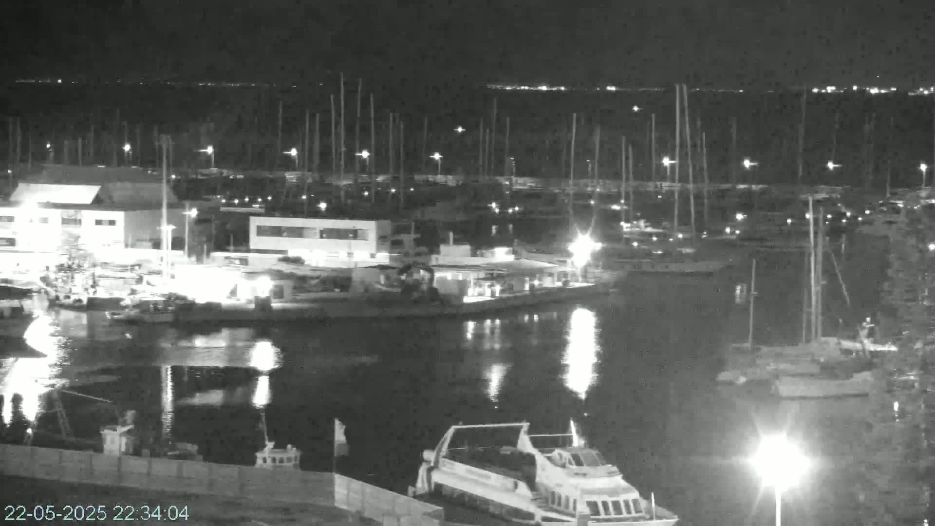 A nighttime, low-light view of a marina filled with numerous boats and yachts, with calm water reflecting the lights.