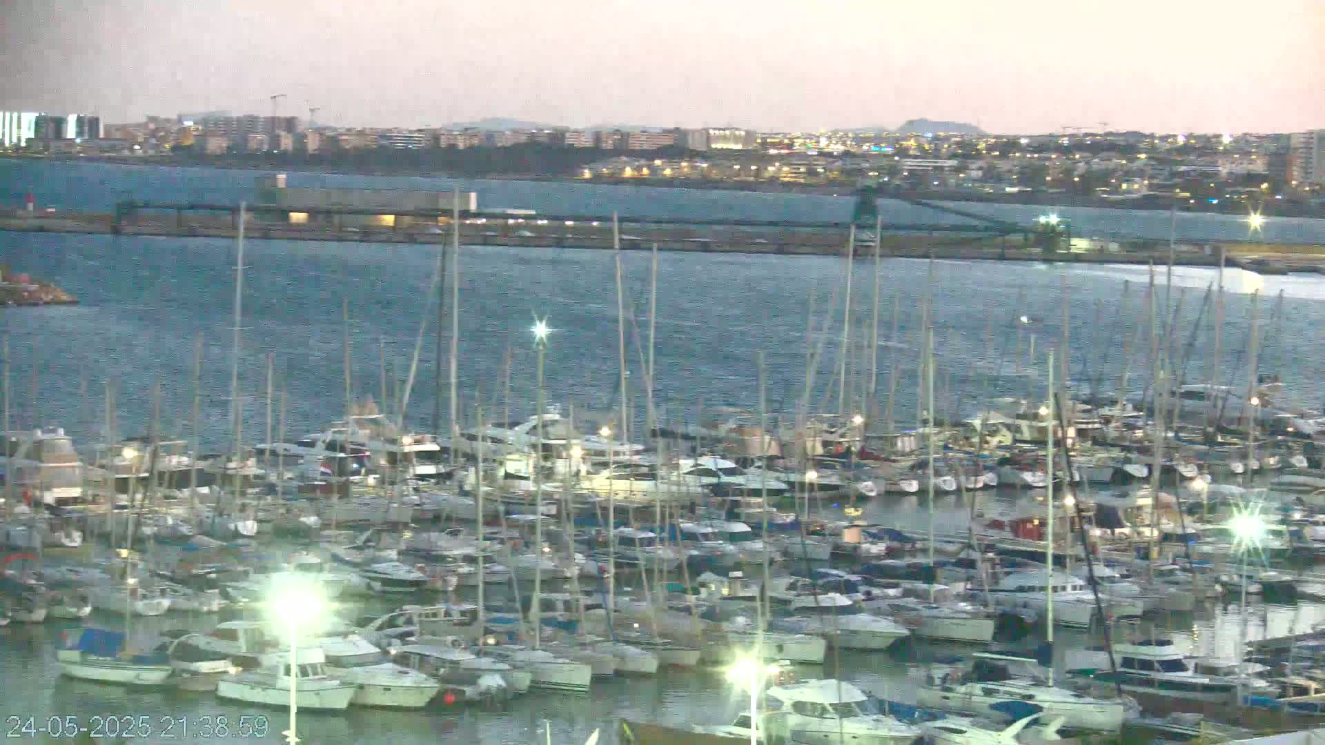 A large marina filled with numerous sailboats and motorboats is situated in front of a city skyline under a dusky sky.