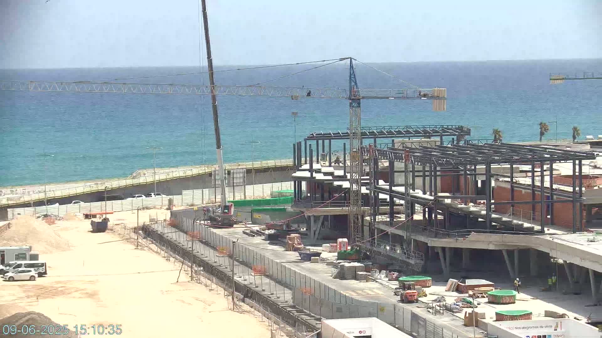 A large building under construction near a calm ocean on a sunny day.