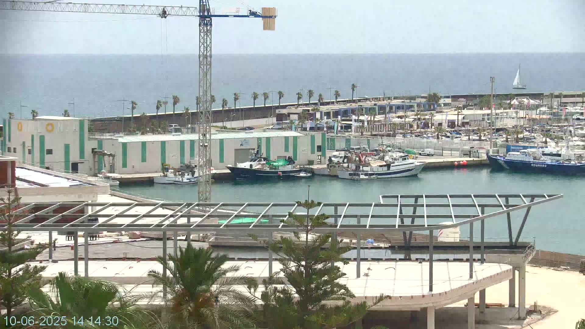 A harbor filled with boats under a mostly clear sky, with a construction crane and a partially built structure in the foreground.