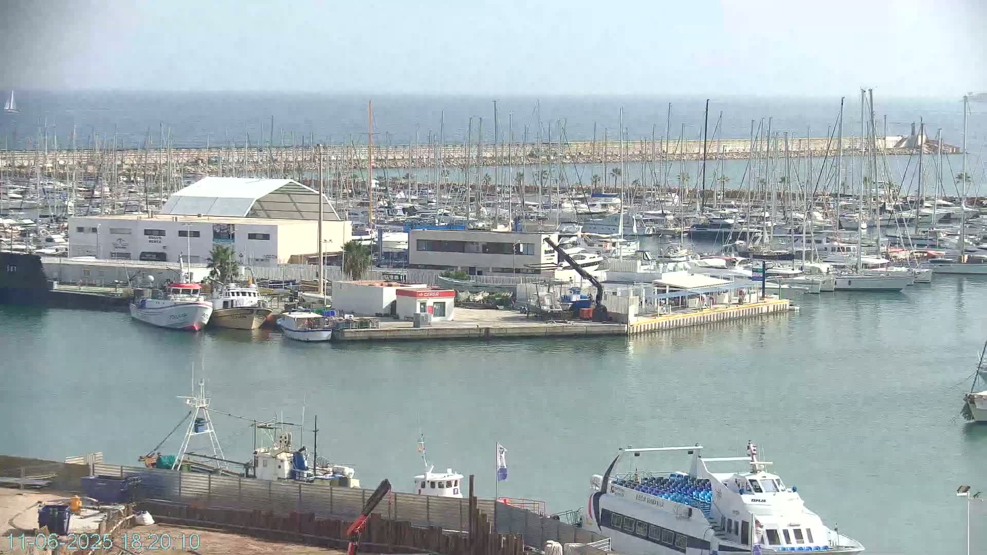 A harbor filled with numerous sailboats and motorboats, some docked and others in the water, under a mostly clear sky.