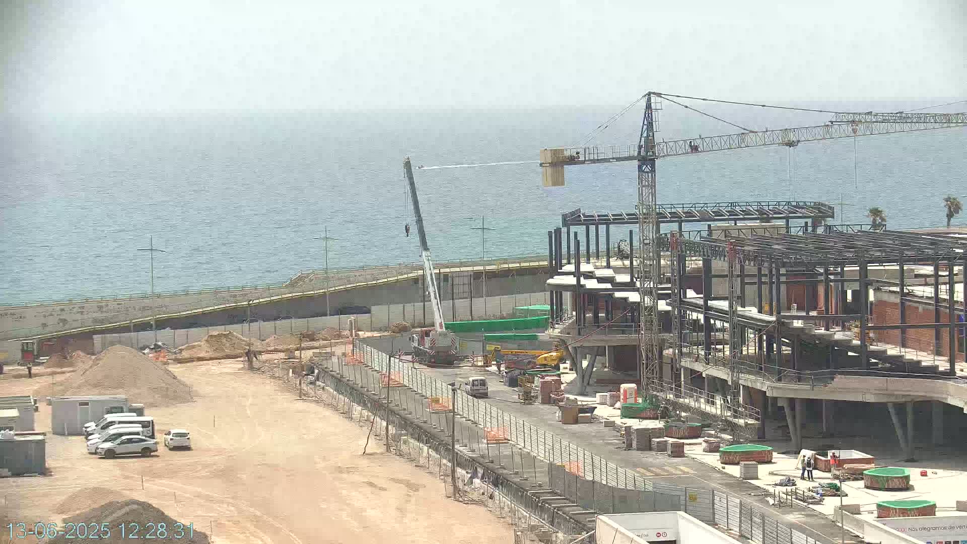 A construction site with two cranes is visible near a body of water under a hazy sky.