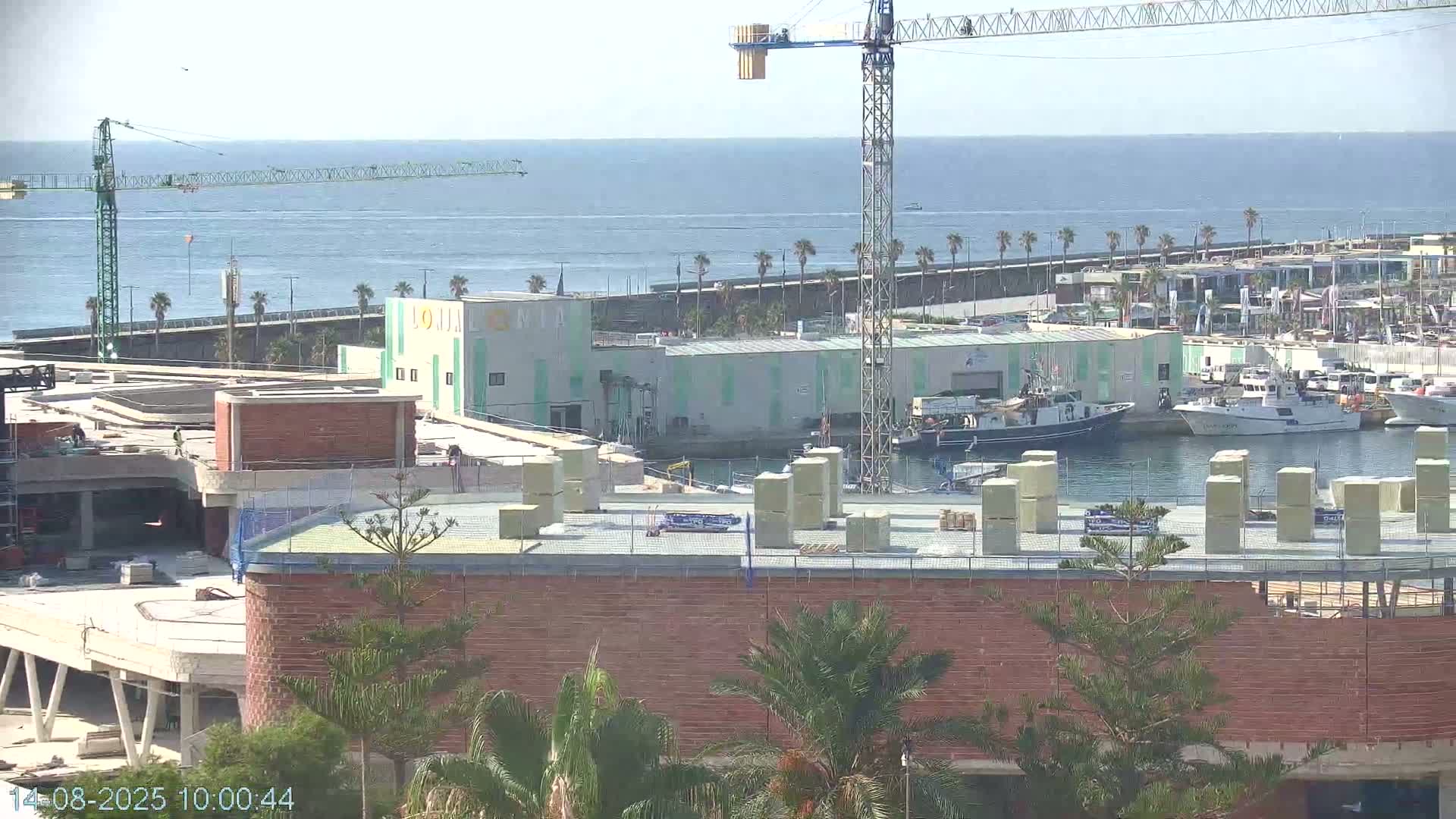 A construction site overlooks a harbor with several boats, a crane, and a clear, sunny day.
