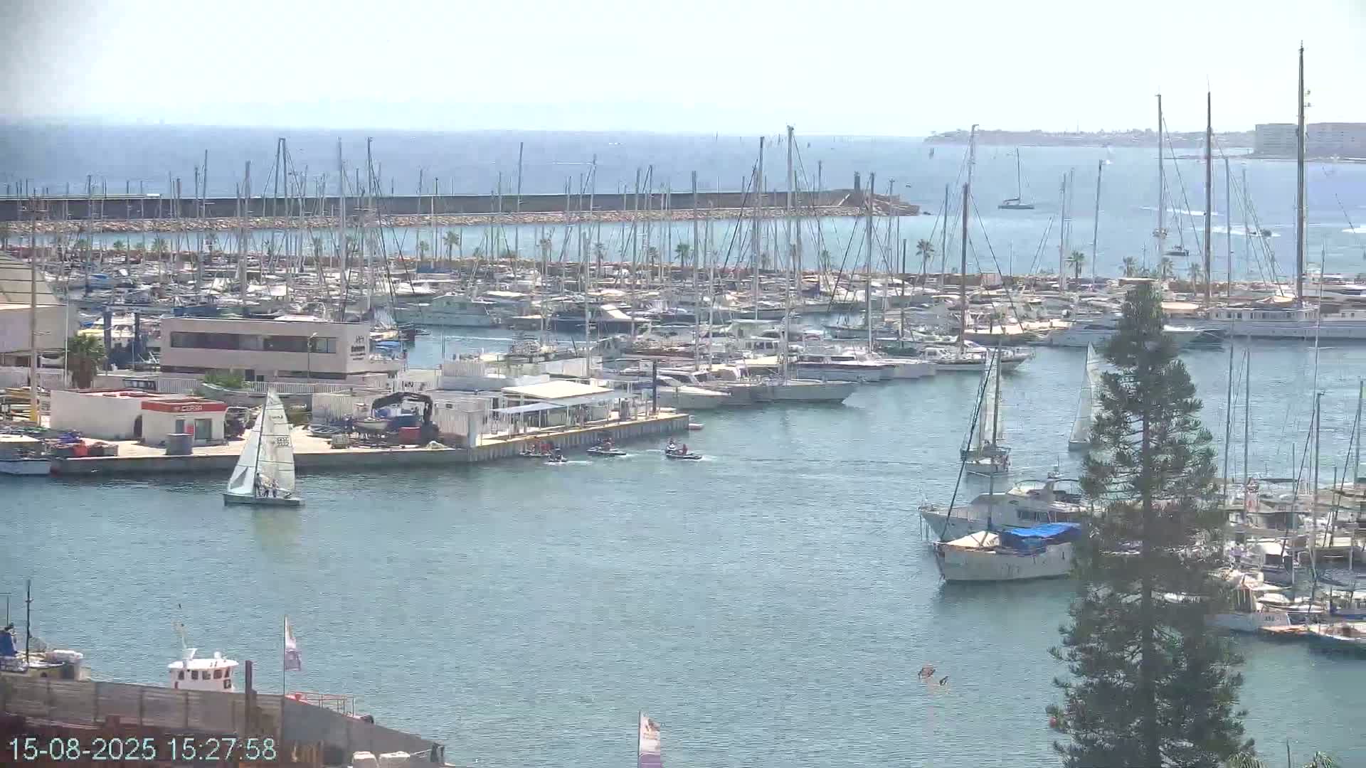 A construction site overlooks a harbor with several boats, a crane, and a clear, sunny day.